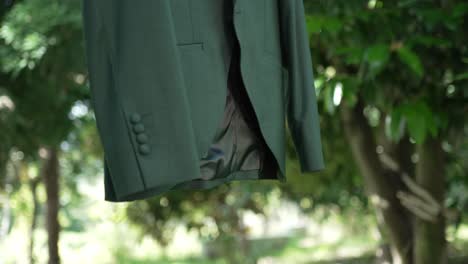 green groom jacket with buttoned sleeve hanging outdoors with sunlight and trees in background