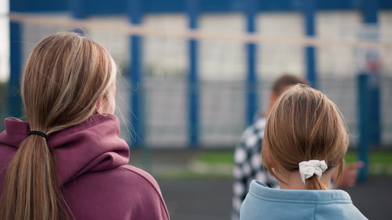 머리카락이 여있는 젊은 여자 배구 선수들의 머리 모습, 검은 리본을 가진 한 명,  리본을 입은 한 명, 코치가 지침을 주고, 강사가 배경에서 움직이는 것을 지켜보고 있습니다.