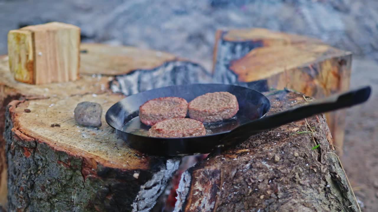 cocina lentamente y fuma tres hamburguesas en una sartén de acero inoxidable en una instalación al aire libre