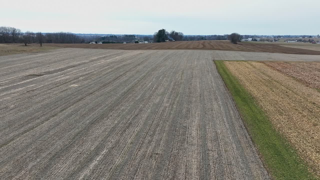 Weite Felder zeigen verschiedene Anbautechniken und Wachstumsstadien der Pflanzen. Die Landschaft wechselt von kargem Boden zu üppiger Vegetation und betont die landwirtschaftliche Vielfalt.