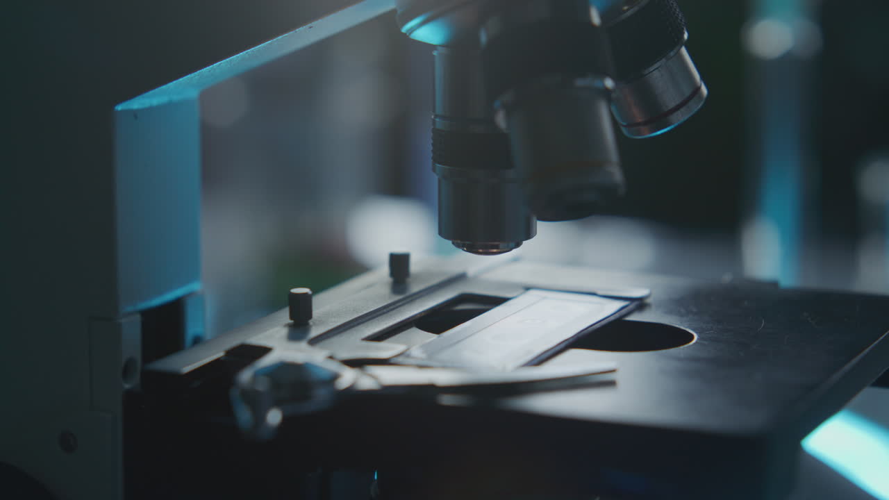 Glass Slide with Specimen Being Moved under Microscope Objective Lens
