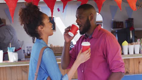 Happy-diverse-couple-talking-and-drinking-takeaway-coffees-by-food-truck