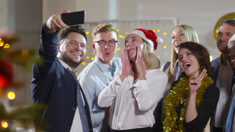 Glückliche-Büroangestellte,-Die-Lametta-Und-Weihnachtsmützen-Tragen,-Grimassen-Schneiden-Und-Selfie-Zusammen-Auf-Der-Weihnachtsfeier-Bei-Der-Arbeit-Machen