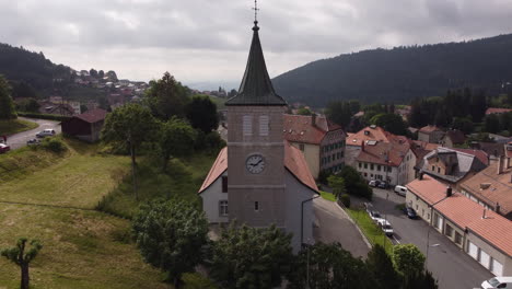Aerial-rise-and-reverse-subject-shot-of-a-church-in-Sainte-Croix,-Switzerland-on-a-cloudy-day