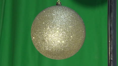 this video shows a gold glitter christmas ornament ball hanging by a string and slowly spinning around in front of a green screen