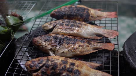 whole fishes is being cooked on metal grid grill at the street near a restaurant in pekin