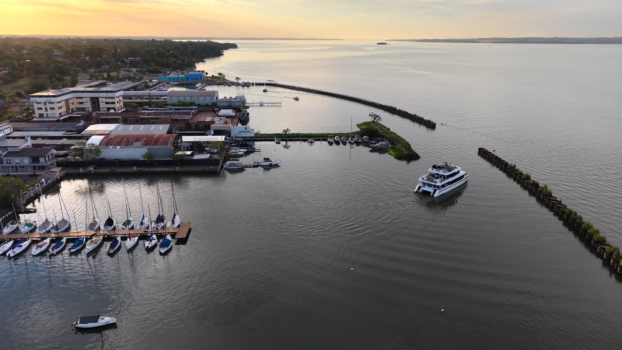 Drone shot of a boat exiting a marina with catamarans and calm water at sunset