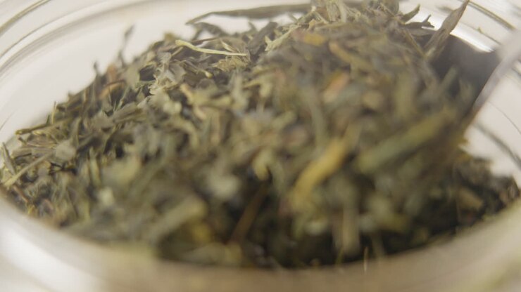 Close-up of spoon taking out a pile of green tea leaves out of a glass jar in 100 FPS