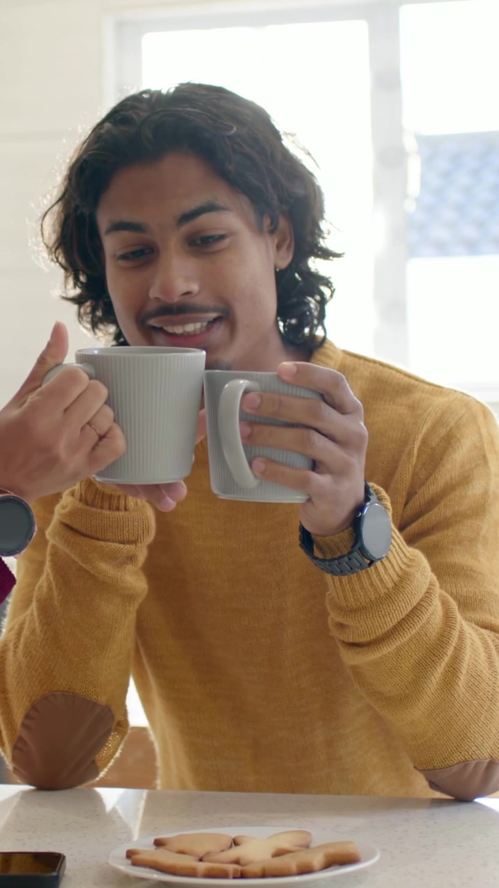 Video vertical: Ofreciendo una taza, hombre con suéter mostaza tomando y oliendo tazas grises en el mostrador