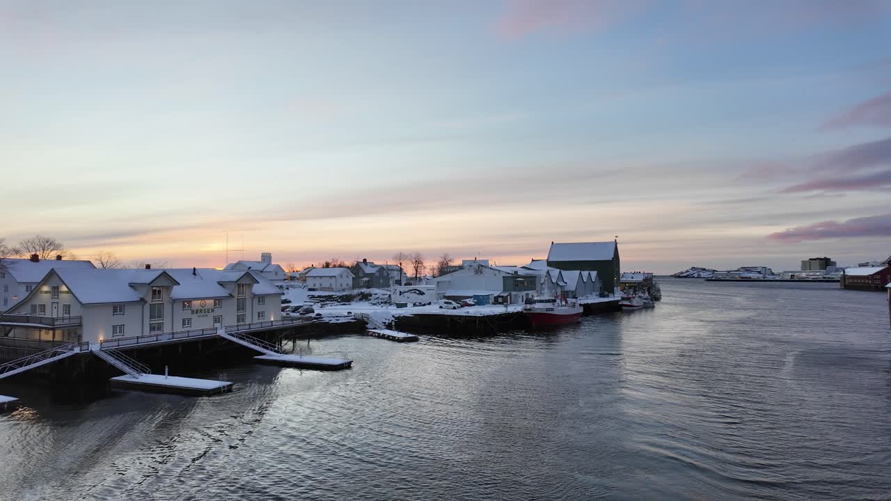 A serene winter harbor scene with snowy houses, boats, and a pastel sunrise sky