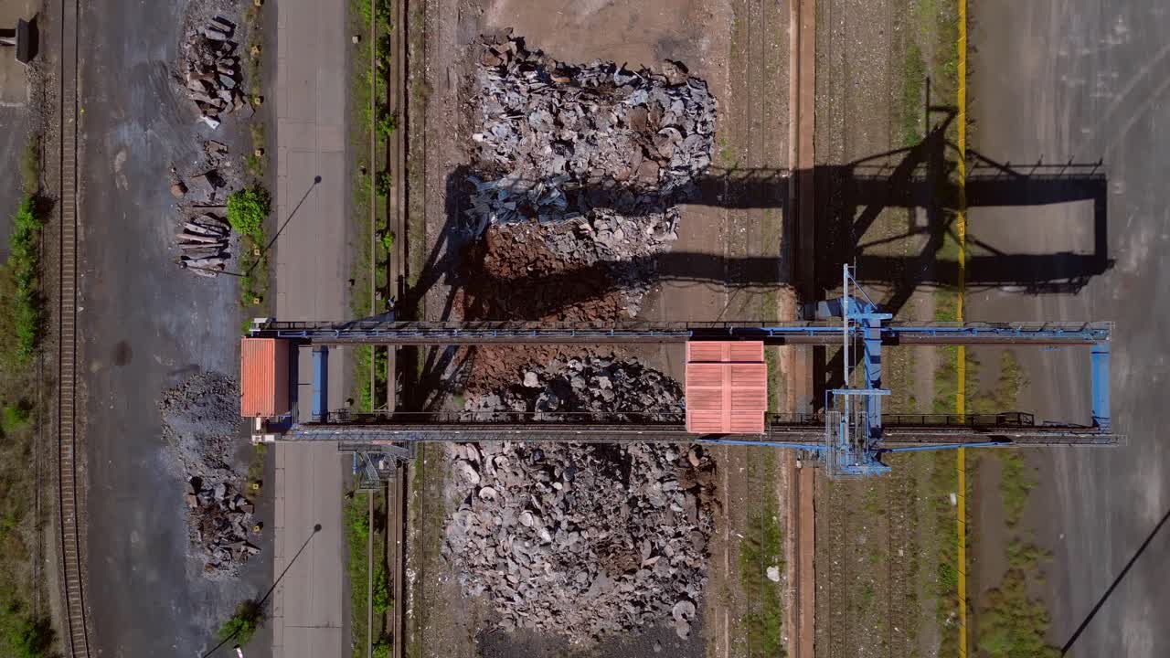 Gantry crane transporting scrap metal at Hennigsdorf electric steel mills on a sunny summer day. Lovely aerial view flight vertical bird's eye view drone rotation to right drone