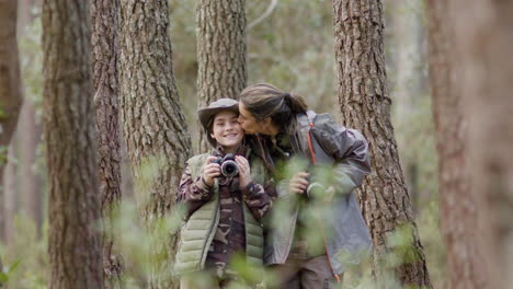 mother and son posing with photos cameras and showing affection while exploring forest