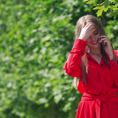 gorgeous young lady with mobile phone. beautiful woman with long hair talking on the phone happily. pretty girl standing near the green tree. slow motion.