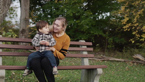 a young mother with a little son sits on a bench in the park