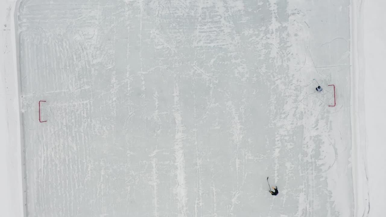 arriba hacia abajo, dos personas jugando hockey sobre hielo en una pequeña pista de hielo en un lago congelado