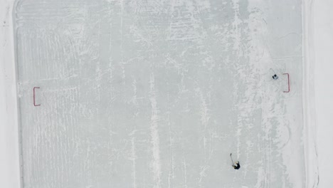 Aerial-top-down,-two-people-playing-ice-hockey-on-small-ice-rink-on-frozen-lake