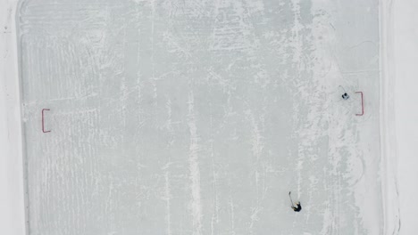 aerial top down, two people playing ice hockey on small ice rink on frozen lake