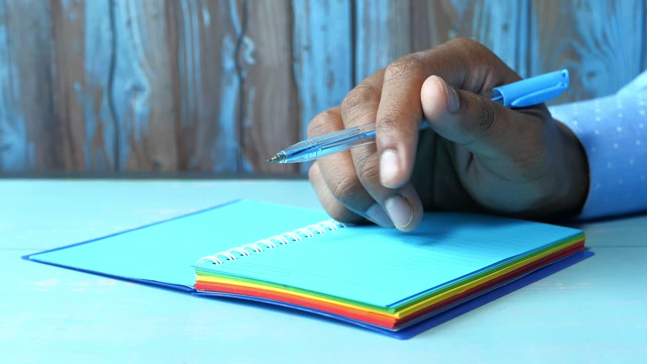 Person writing in a colorful spiral notebook