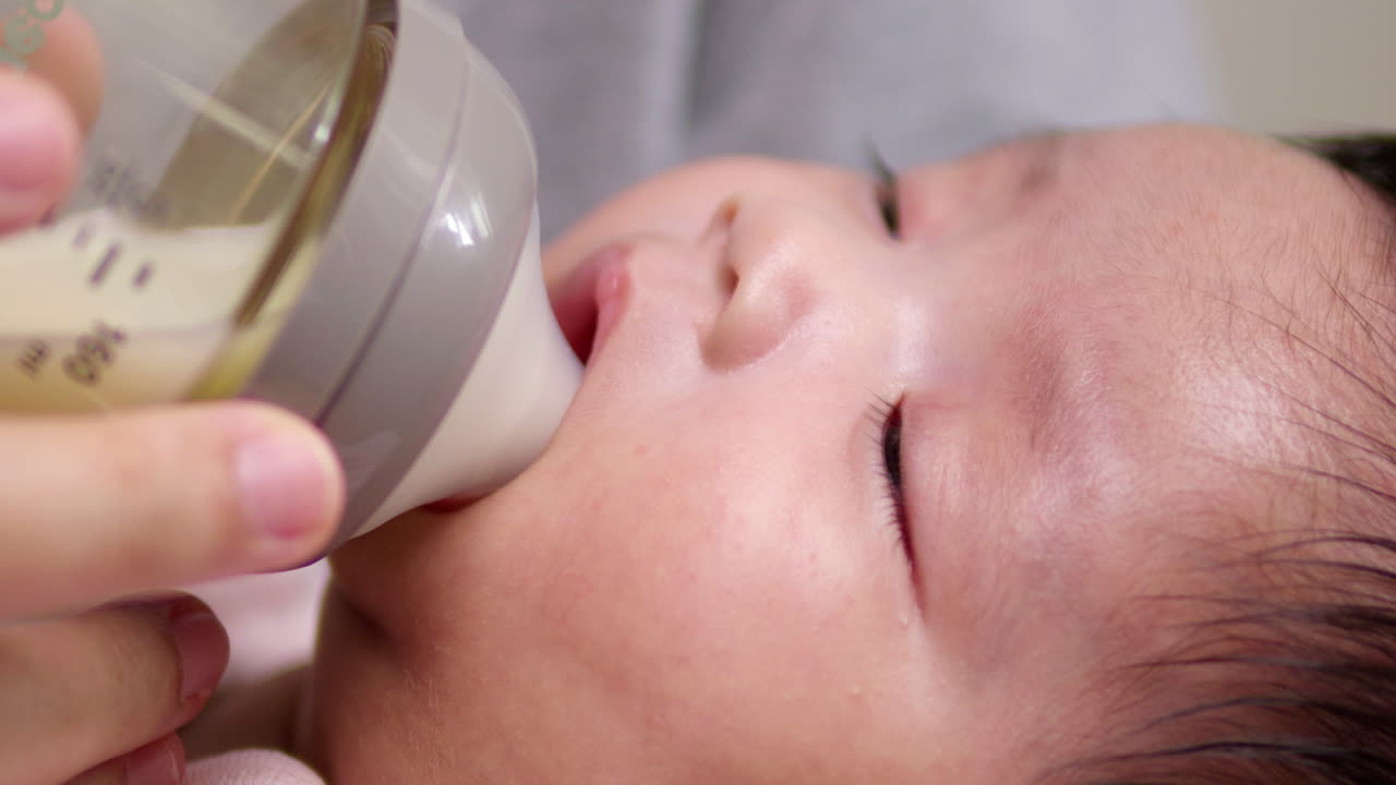 A sleeping newborn child is latching on to a baby feeding bottle while it drowses off to sleep.