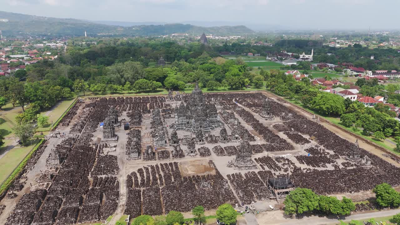 Right orbit drone circles Sewu Temple within the Prambanan complex near Yogyakarta, Indonesia, revealing symmetrical ruins, stone stupas and the central shrine amid green grounds under clear sky