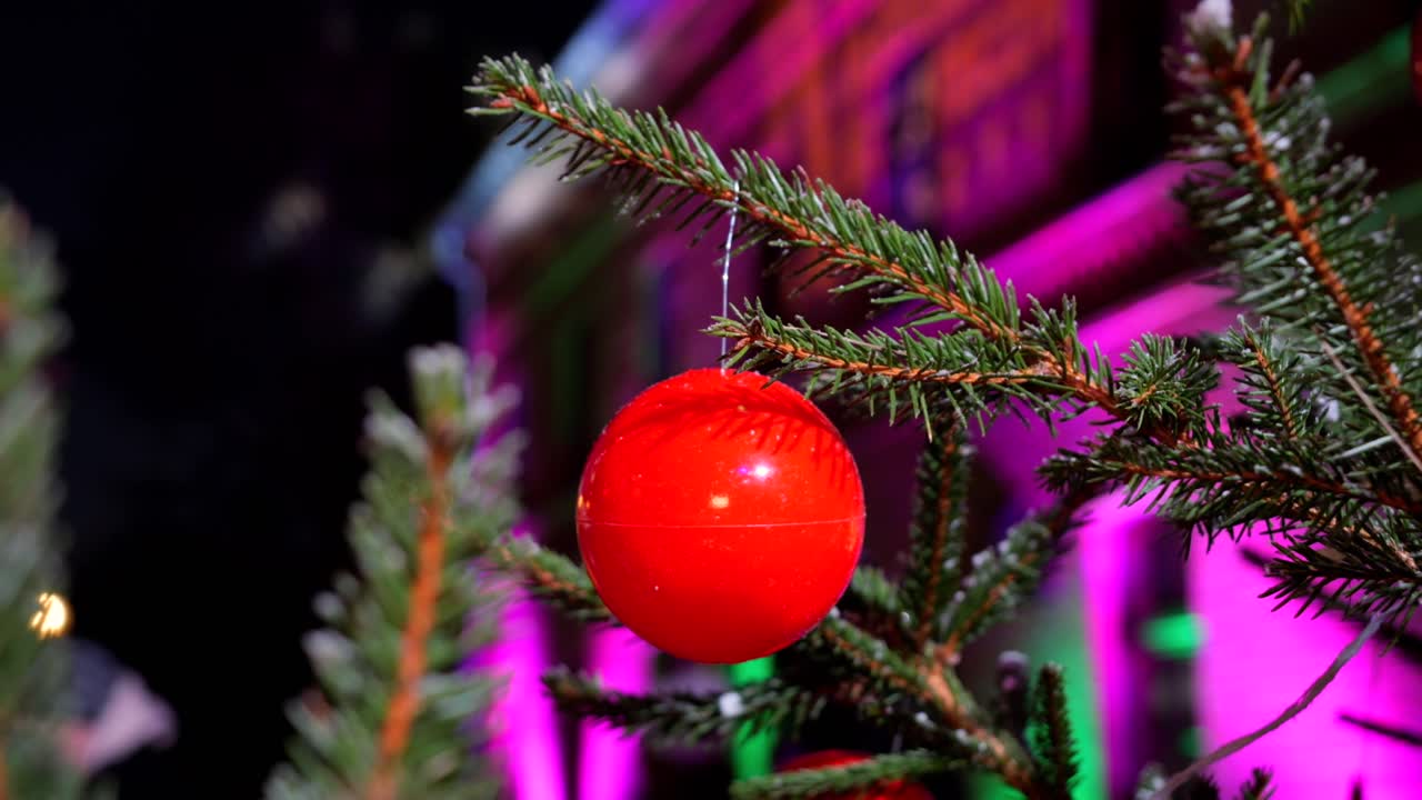 una vista de una bola de plástico roja colgando de un árbol de navidad cubierto de nieve