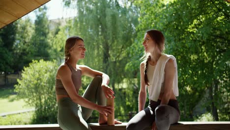 a blonde girl and a brown-haired girl are talking against the backdrop of a beautiful green forest sitting in a gazebo. leisure and communication in nature