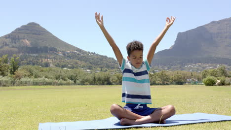 biracial boy practices yoga outdoors, with mountains in the background, in school