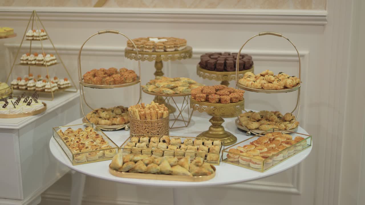 Elegante tavola imbandita con un assortimento di pasticcini, torte e dolci disposti su alzate dorate durante un ricevimento.