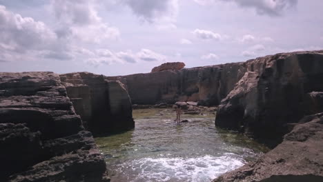 Long-haired-nude-caucasian-man-poses-in-natural-rock-pool-Ibiza,-drone