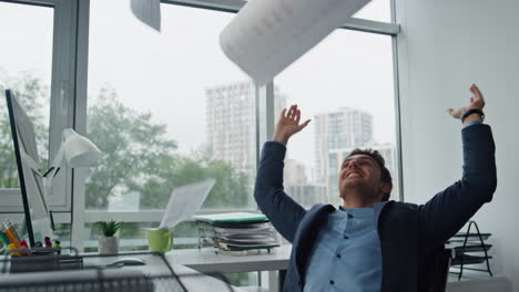 smiling businessman throwing papers at glass workplace. happy manager celebrate