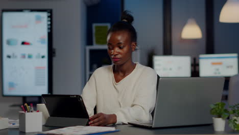 Mujer-Gerente-Africana-Usando-Una-Computadora-Portátil-Y-Una-Tableta-Al-Mismo-Tiempo-Trabajando-Horas-Extras