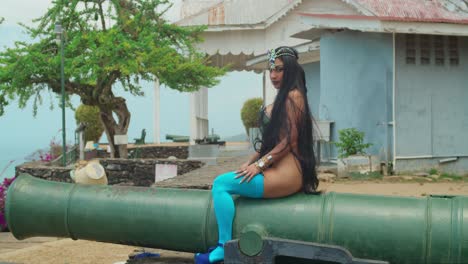 a spirited young woman, donning a vibrant carnival costume, takes a seat on a cannon at a historic fort