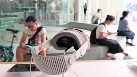 the apple vision pro, the brand's mixed-reality headset, is prominently displayed in the foreground, while customers can be seen in the background at the apple store.