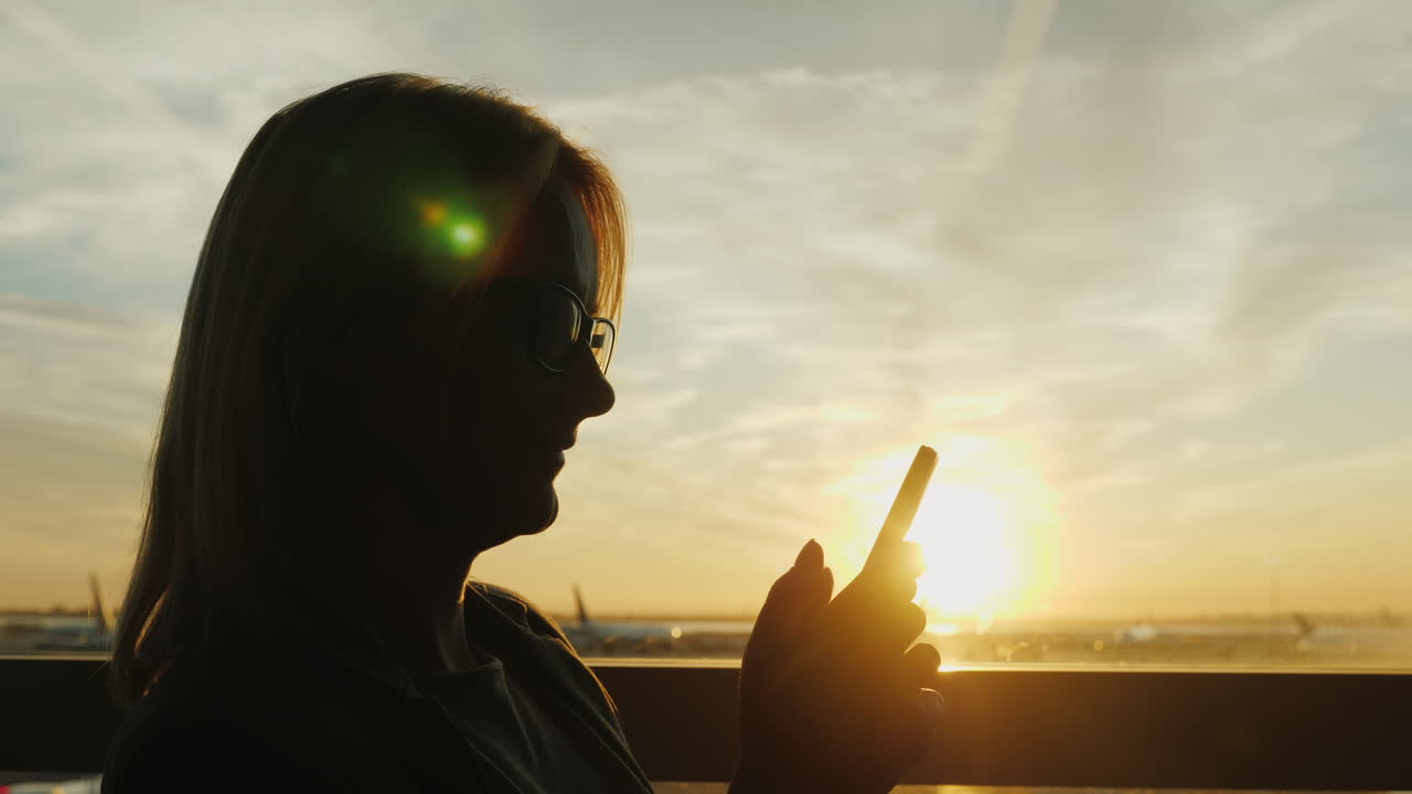 женщина пользуется смартфоном в аэропорту на закате