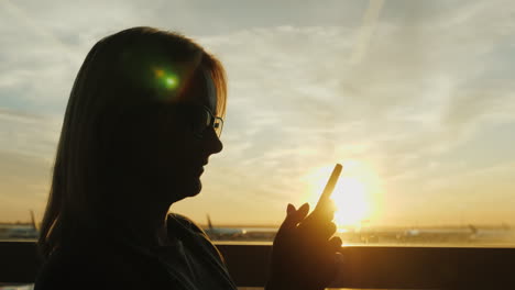 woman uses smartphone in airport at sunset