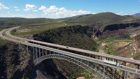 un dron de 4k retrocede sobre el puente burro creek en wikieup arizona en un día soleado con cielos azules y parches de nubes blancas, tráfico conduciendo sobre el puente