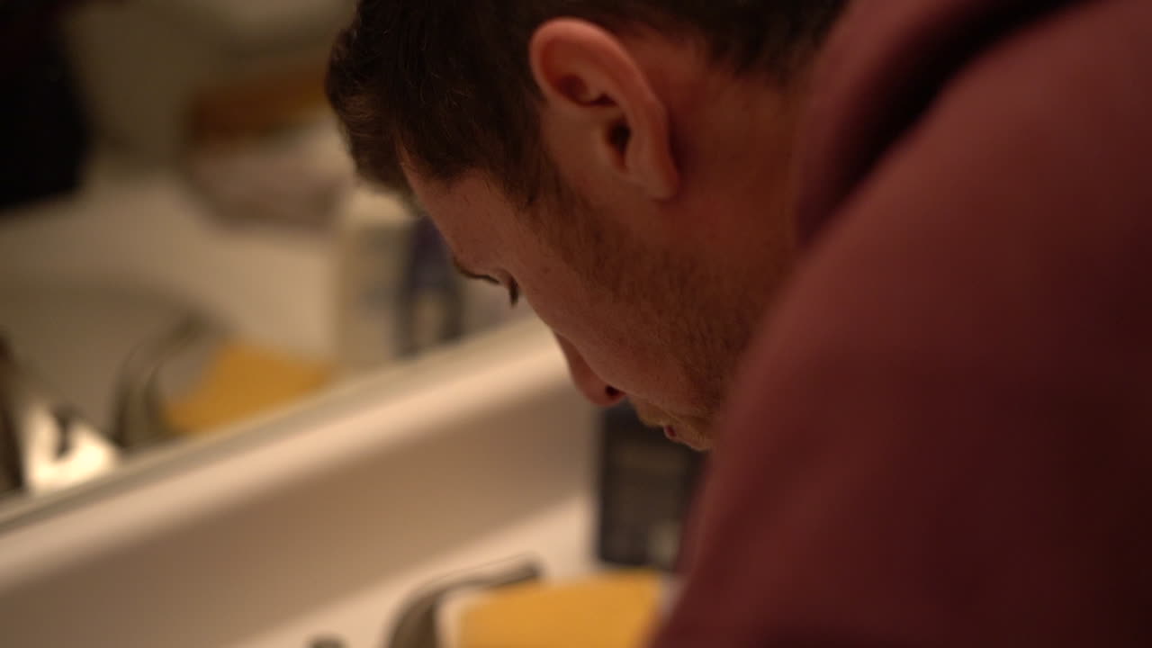 hombre adulto joven cepillándose los dientes en el lavabo del baño - aislado