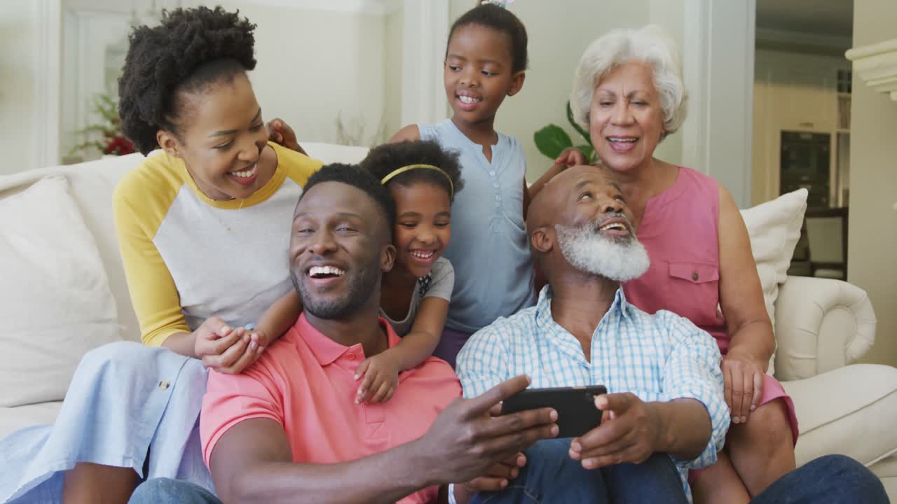 Happy african american family sitting and using smartphone in living room
