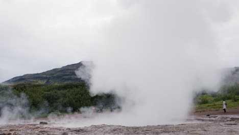 turistas irreconocibles viendo un géiser en erupción de agua, islandia