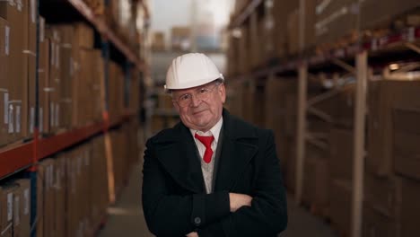 portrait of a solid elderly man in a business suit with a helmet on his head on the background of the composition with cardboard boxes