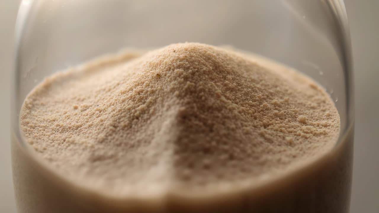 Displaying fine beige powder piled inside clear glass jar on kitchen countertop, pantry storage
