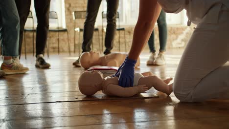 Close-up-shooting:-A-professional-nurse-in-a-white-medical-uniform-teaches-a-group-of-people-first-aid-and-demonstrates-cardiopulmonary-resuscitation-techniques-using-a-baby-dummy.-Medical-training-session