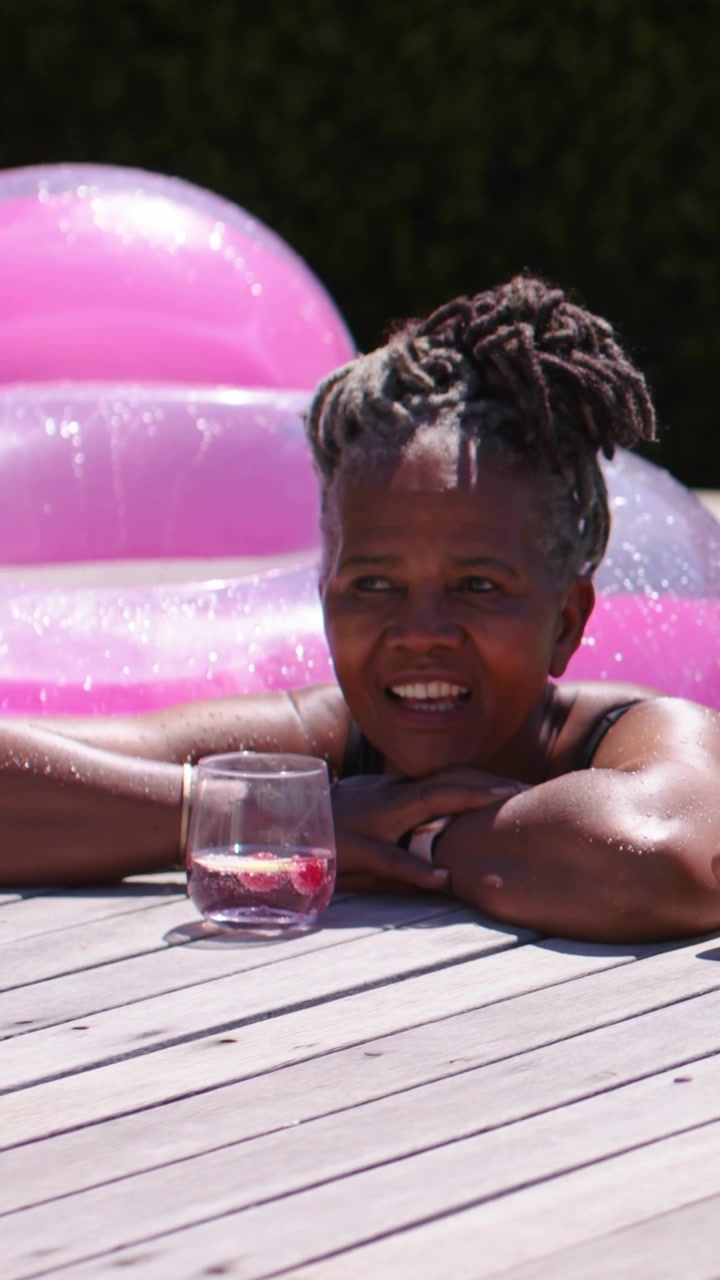 Vertical video: Smiling lady in swimsuit blowing and waving at pool, arm entering, pink float near