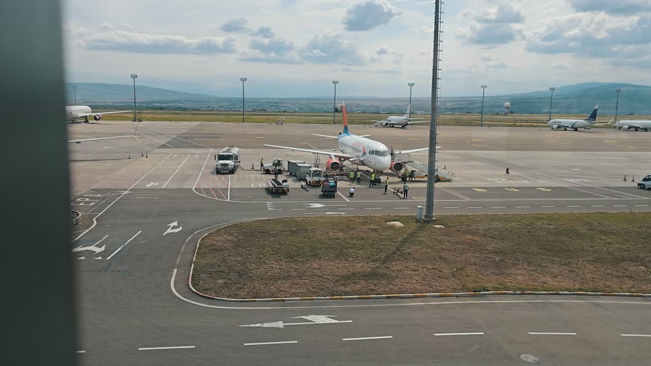 An airplane being serviced by ground crew on the tarmac at a bustling airport