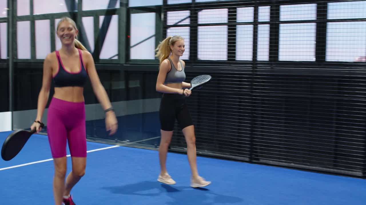 Women enjoying padel tennis match, laughing and chatting on indoor court