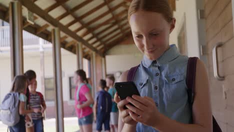 chica usando un teléfono inteligente en el pasillo de la escuela