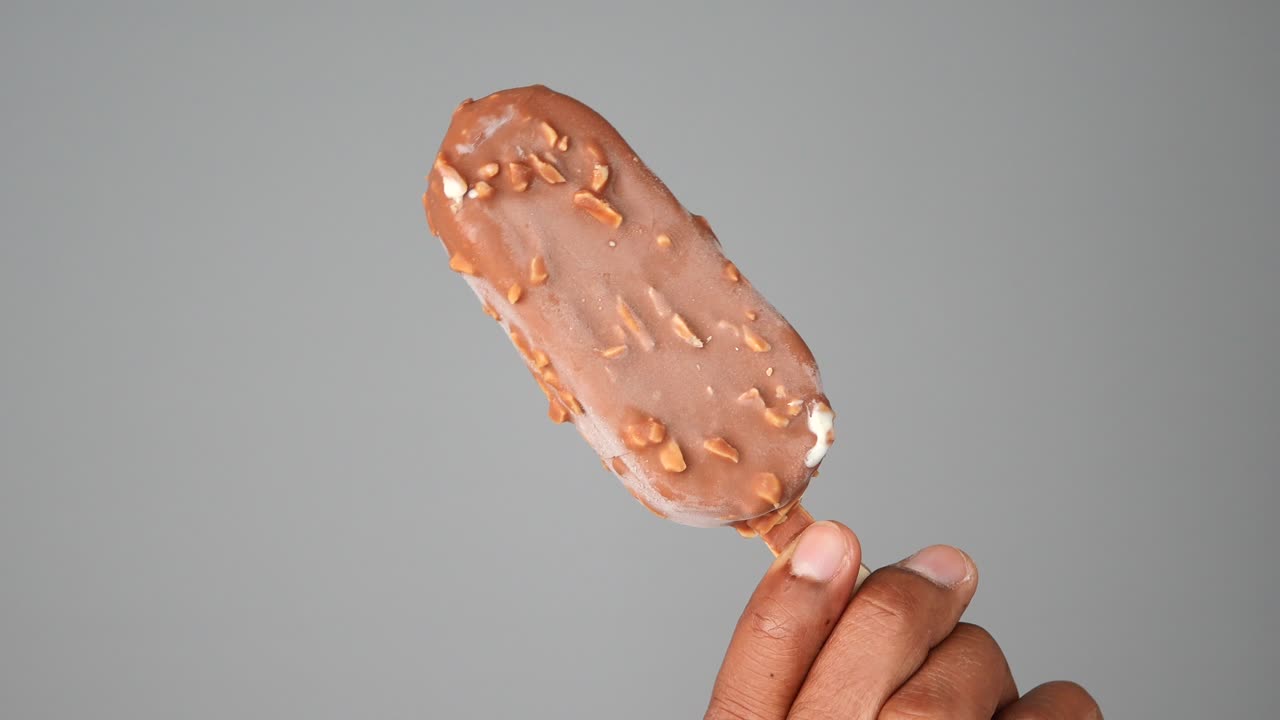Hand holding a chocolate-covered ice cream bar with nuts