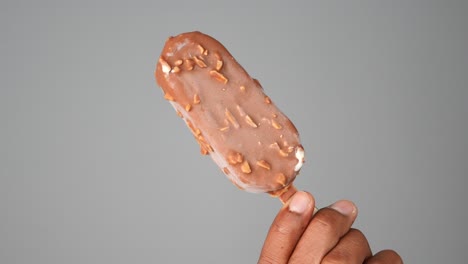 hand holding a chocolate-covered ice cream bar with nuts
