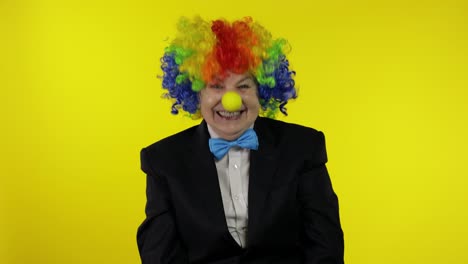 senior old woman clown in colorful wig smiling, fool around, laughing. halloween