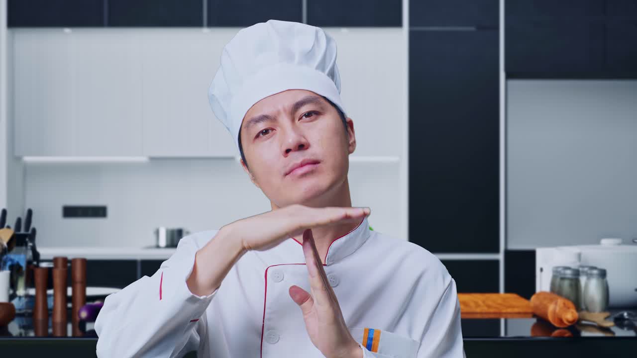 primer plano de un cocinero asiático mirando a la cámara y mostrando el tiempo de salida manos gesto mientras está de pie en la cocina de casa